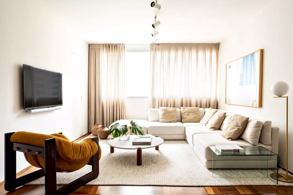Poucos e bons móveis, como o sofá em L desenhado pelo escritório Studio Matuti, que assina o projeto do apartamento, trazem visual minimalista, porém, confortável — Foto: Fran Parente / Divulgação