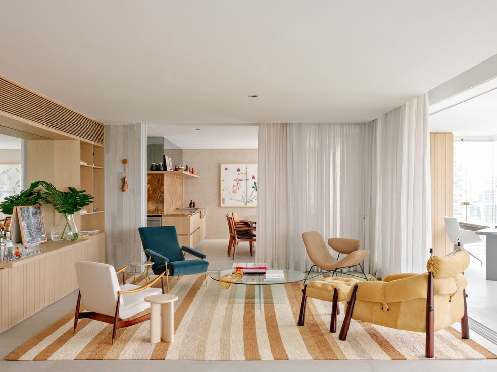 No lugar de sofás, o ambiente tem um mix de poltronas vintage e contemporâneas, como a azul, modelo "D.153.1", do designer italiano Gio Ponti para Molteni; a poltrona "Reversível", do designer austro-argentino Martin Eisler (à direita, ao fundo); e a poltrona com pufe "MP81", do brasileiro Percival Lafer (à frente), adquirida em antiquário. Tapete listrado feito sob encomenda pela by Kamy. Cortinas com tecido JRJ executadas pela Dauer Decor. Projeto do arquiteto Alexandre Dal Fabbro — Foto: Fran Parente/Divulgação