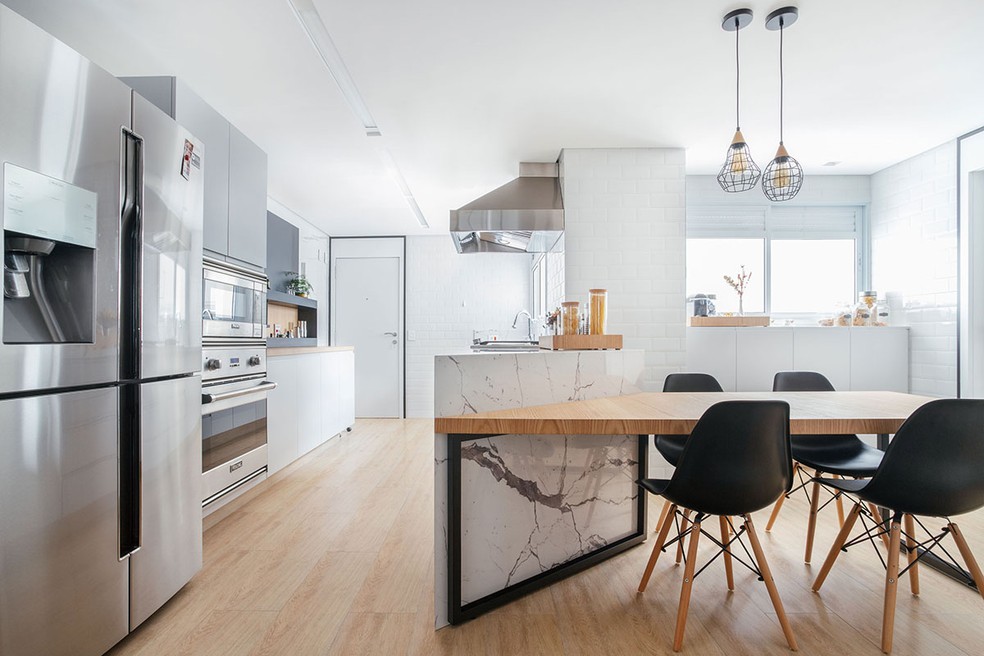 A cozinha tem uma mesa para almoço, que fica diretamente conectada à bancada. Projeto do escritório ISE Arquitetura — Foto: Maura Mello / Divulgação