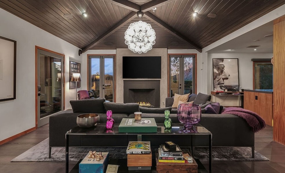 A sala de estar tem um sofá grande e portas de vidro — Foto: Douglas Elliman / Reprodução