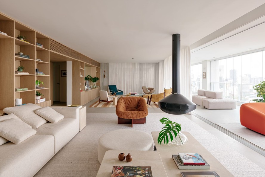 LIVING INTEGRADO | No espaço conectado, a poltrona vintage PL 61, de Percival Lafer, está ao lado da lareira suspensa da Construflama. O conjunto de mesas de centro, desenhadas pelo escritório e executadas com Limestone, ganhou um pufe redondo seguindo o mesmo tecido do sofá. Tapete da by Kamy. A varanda integrada em formato retangular foi idealizada para vários usos, como contemplação da vista da cidade