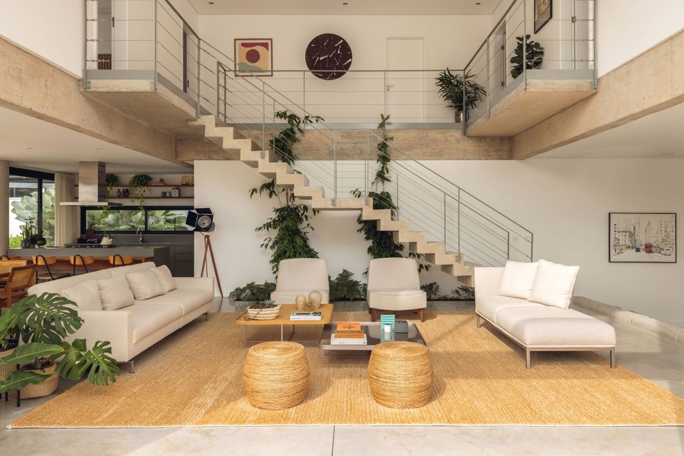 SALA DE ESTAR | A escada feita em concreto moldado 'in loco' se tornou uma peça escultórica no centro do ambiente, envolta por trepadeira-castanha. Sofás da Lider Interiores. Tapete com aspecto de palha da by Kamy — Foto: Maura Mello/Divulgação