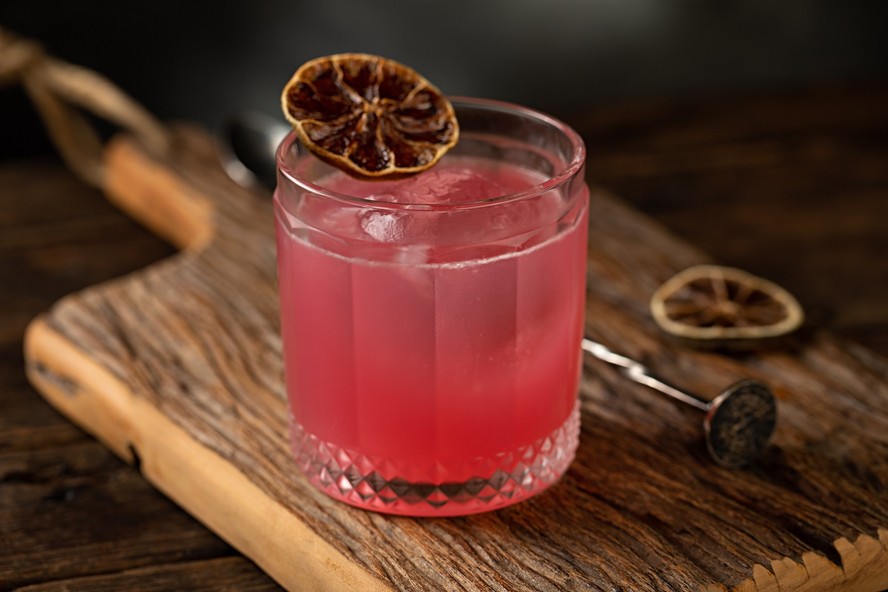 Receita de drinque rosa com gin, xarope de toranja e limão é decorada com uma fatia de limão desidratado