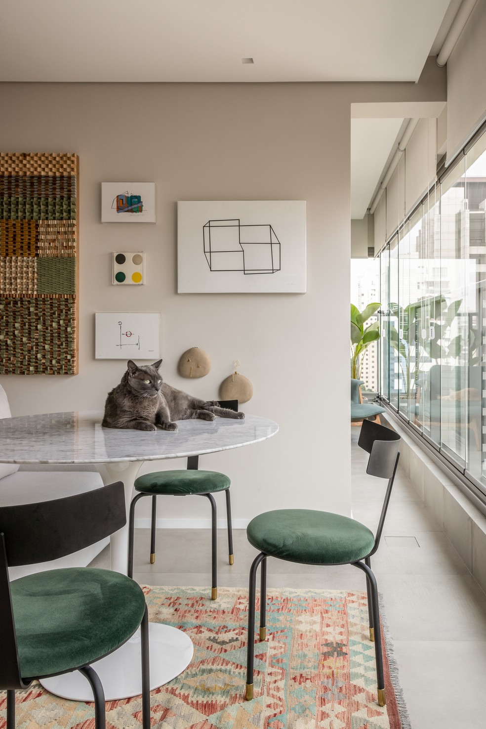 ESPAÇO GOURMET  | A gallery wall foi composta com obras de diversos artistas. Os gatos podem acessar todos ambientes da casa e no jantar, um deles aproveita a iluminação natural em cima da mesa. As cadeiras verde trazem um ponto de cor para a decoração — Foto: Evelyn Müller / Divulgação