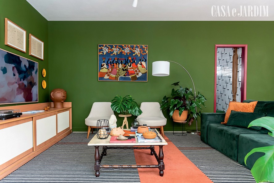 No apartamento da arquiteta Sthepanie Ribeiro, a tapeçaria vintage inserida na sala de tons vibrantes é valorizada com a parede pintada em verde escuro