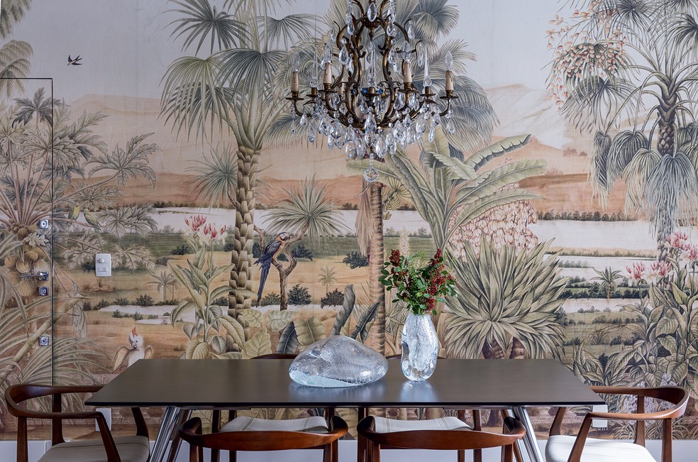 SALA DE JANTAR | Destaque para o papel de parede com motivos tropicais, junto à sala de jantar, e o lustre francês de cristal — Foto: Arq.verso/Divulgação