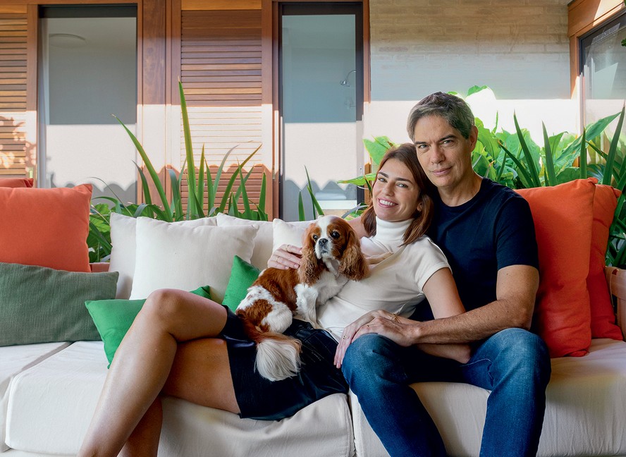 RETRATO | O jornalista Ricardo Amorim e a esposa Fernanda estão na varanda, sentados com a cadela Petite no sofá da Schuster, próximos à mesa de centro da Breton