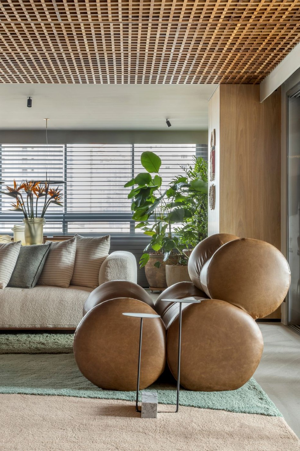 ÁREA SOCIAL | Na sala de estar, um espaço de relaxamento é composto por poltrona Fardos, de Ricardo Fasanello, acompanhada pela mesa lateral Adobe, de Guilherme Wentz, na loja Via Condotti. O paisagismo da Vaso e Cia, com plantas como maranta-charuto e jiboia gigante, traz uma atmosfera natural ao ambiente. Cortina Silhouette, da Hunter Douglas, na Bela Arte — Foto: Edgar Cesar/Divulgação