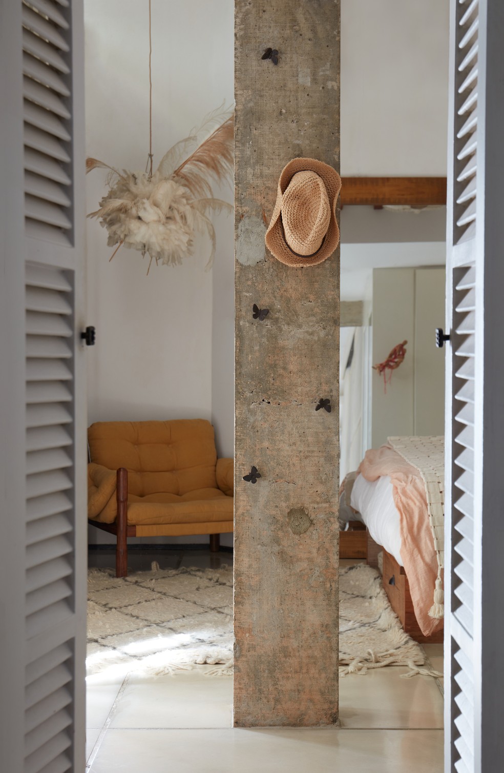QUARTO | O pilar do quarto tem pequenos penduradores para apoiar objetos. Poltrona mostarda é da Verniz SP — Foto: Paula Chaffin / Divulgação