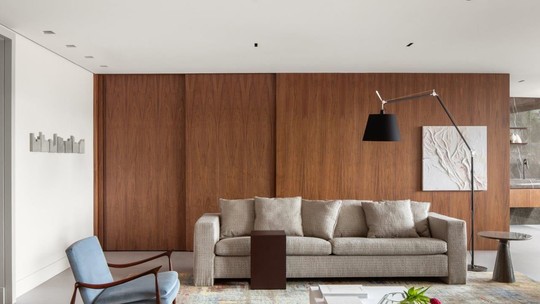 Tons neutros e painéis de madeira conferem clima sóbrio em apartamento