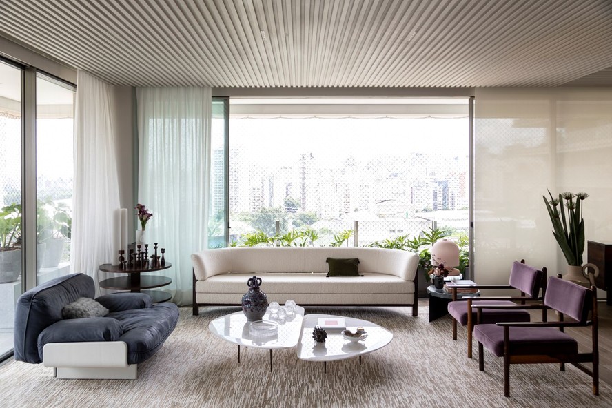 SALA DE ESTAR | Com vista para a cidade de São Paulo, o ambiente tem sofá arredondado com desenho de Arthur Casas, na Etel Interiores, revestido com tecido da Dedar. Poltrona azul e branca da Baxter Furniture, comprada na Casual Móveis. As poltronas roxas, de Jean Gillon, que pertenciam a um hotel que foi fechado, foram adquiridas no antiquário Thomaz Saavedra. Mesa de centro, design de Simone Costi, na Firma Casa. Mesa lateral, de Gregori Warchavchik, na Etel Interiores. Tapete da By Kamy. Paisagismo assinado por Mera Arquitetura Paisagística