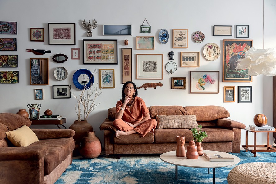 RETRATO | Calu Fontes está na sala. Almofada e pufe de palha da Codex Home, assim como a mesa de centro, com trio de vasos da Dpot Objeto. À esquerda, vasos de barro da Casa Atica. À direita, banco 'Pequi', do designer Dan Azvdo para o Behavez Studio, da Deezign. Tapete azul da By Kamy. O sofá já era da moradora