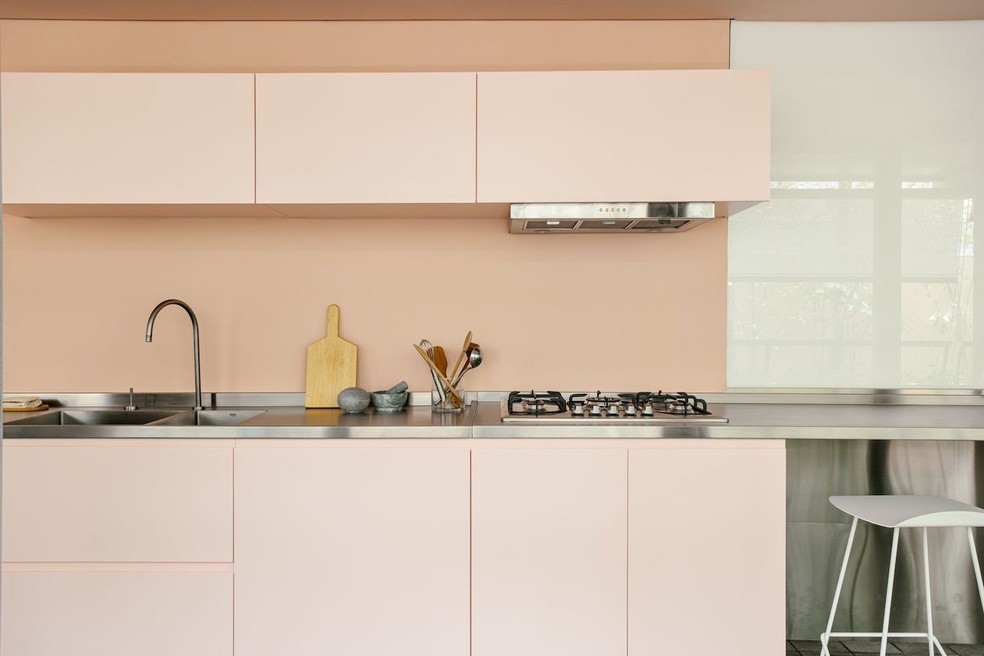 A cozinha possui marcenaria, paredes e teto pintados de rosa claro, contrastando com os tons neutros e gradações de cinza predominantes em quase todo o apartamento — Foto: Idea!Zarvos / Divulgação