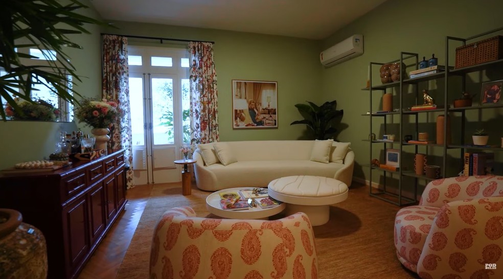 A sala de estar tem um sofá branco e poltronas estampadas, que combinam com a cortina — Foto: Youtube/ Reprodução