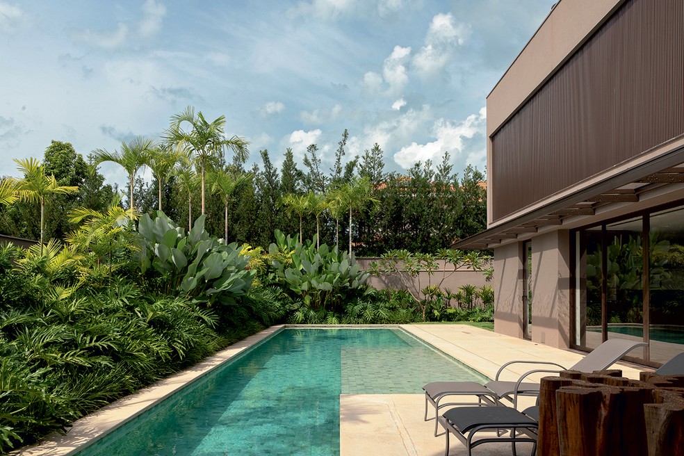 ÁREA EXTERNA | Casa projetada por Storrer Tamburus Arquitetura, com paisagismo de Mônica Costa. Ao fundo, palmeiras carpentárias, maranta-charuto e jasmim-manga criam um horizonte verde. Piso atérmico da Castellato e, na piscina, pastilhas da Atlas — Foto: Keniche Santos / Divulgação