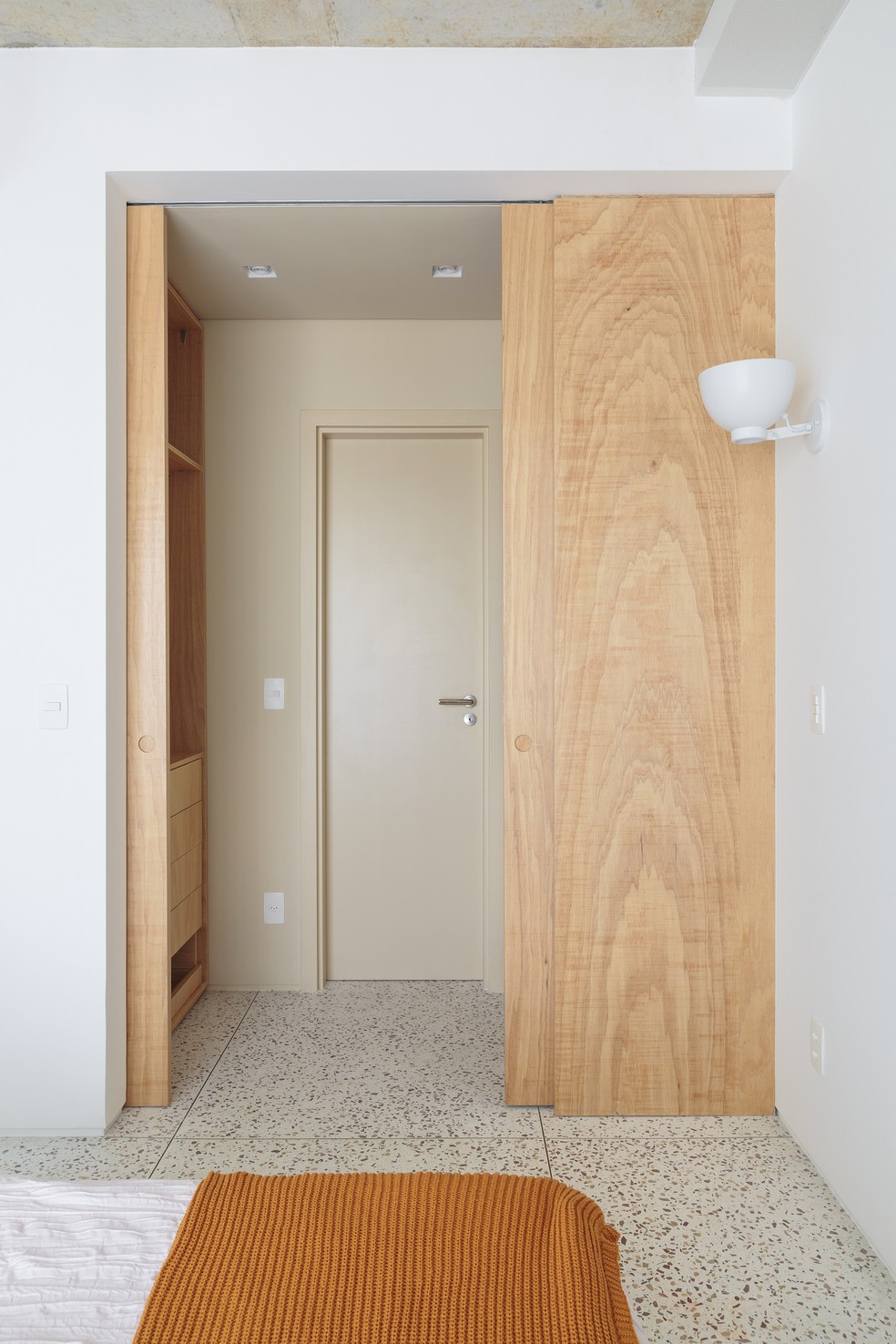 QUARTO | O acesso ao pequeno closet e ao banheiro é feito por uma painel de madeira, que embute portas de correr. Toda a iluminação do apartamento é da Reka — Foto: Felco / Divulgação