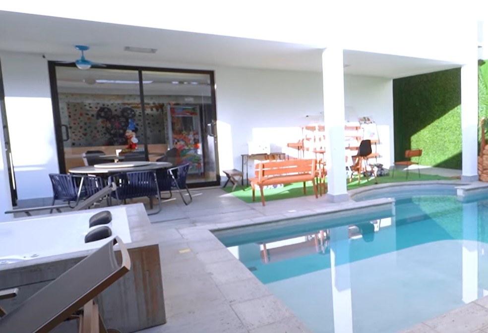 Na área externa da casa, há uma piscina, banheira e mais uma mesa redonda com algumas cadeiras — Foto: Youtube / Reprodução