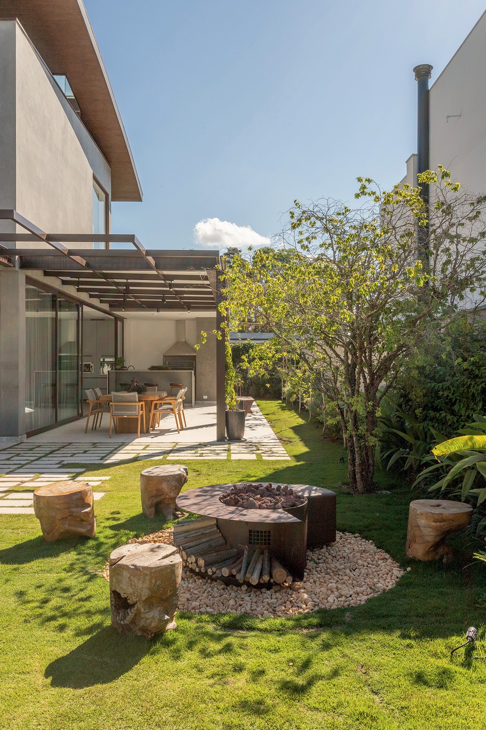 Próximo à jabuticabeira, fogo de chão idealizado pelo SP Arquitetos com tocha interna da Construflama e seixos Campos do Jordão. Bancos da Bali Móveis Rústicos. Ao fundo, sapatinho-de-judia em vaso conduzido por malha metálica — Foto: Leandro Moraes / Divulgação