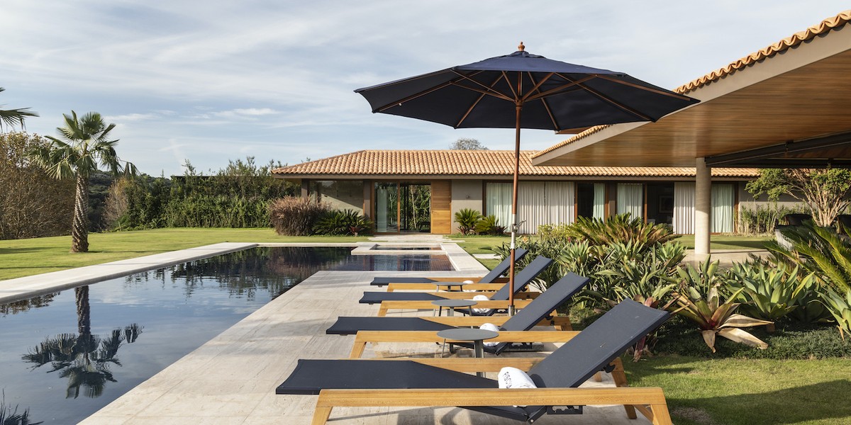 Casa de 810 m² em forma de L abraça grande jardim central com piscina