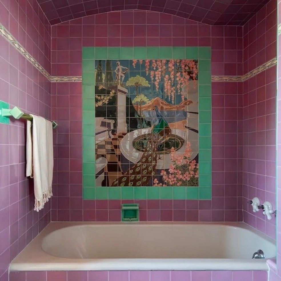 Um dos banheiros tem azulejos na cor rosa e um quadro acima da parede da banheira — Foto: Robb Report / Instagram / Reprodução