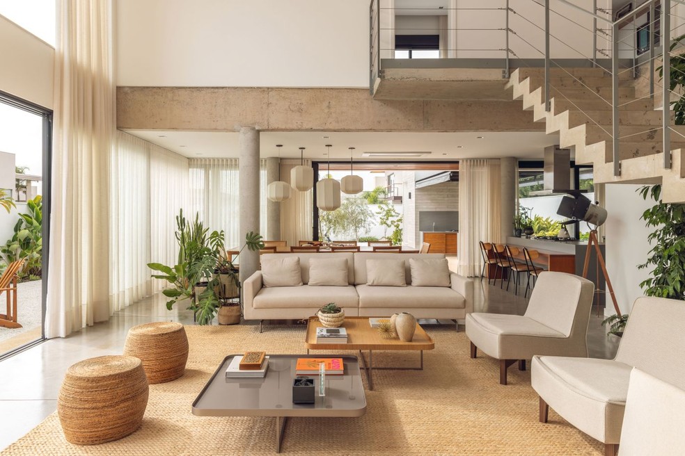 LIVING INTEGRADO | O espaço com conceito aberto reúne sala de estar, de jantar e cozinha, além de se conectar com a área externa por grandes esquadrias de vidro, o que valoriza a luz natural. O design marca a decoração, como as mesas de centro Edge, da Lider Interiores, e o conjunto de luminárias pendentes Lanterna, de Cristiana Bertolucci, acima da mesa de jantar, também da Lider. Ao lado do sofá, costela-de-adão, guaimbê e helicônia marcam o ambiente — Foto: Maura Mello/Divulgação