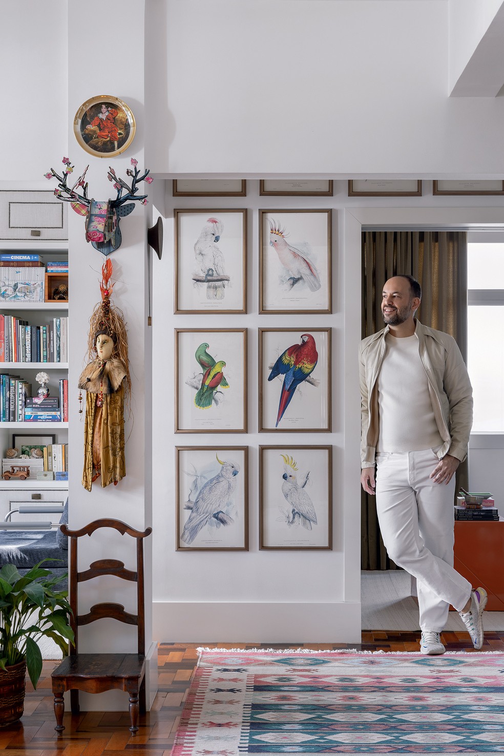 RETRATO | O morador, Marcelo Salum, está em parte do living. Na parede, destacam-se imagens emolduradas de pássaros da coleção The Parrots, da Taschen. A antiga cadeira pertence ao acervo dele, e o tapete é da Oriente Se — Foto: Arq.verso/Divulgação