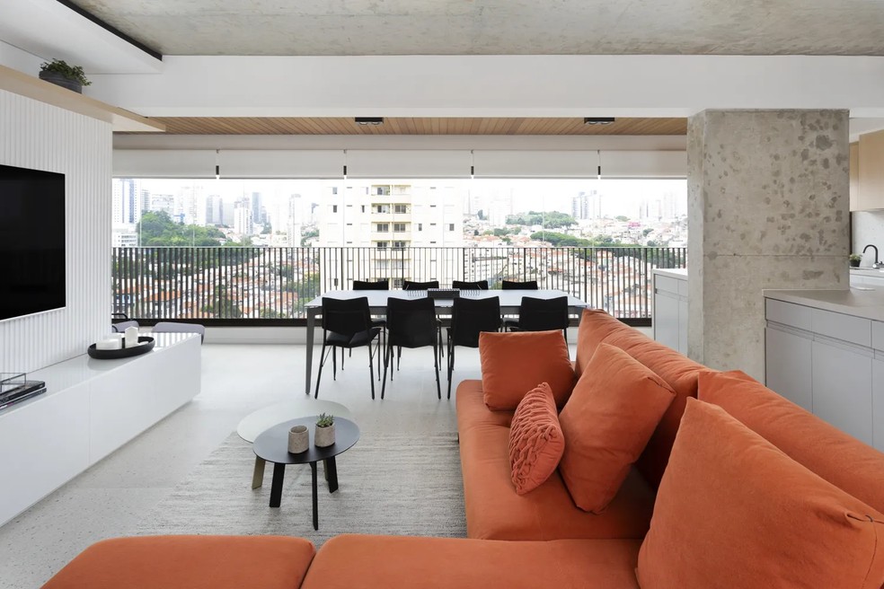O grande sofá laranja em L é o destaque da sala projetada pelo escritório Degradê Arquitetura — Foto: Júlia Ribeiro / Divulgação
