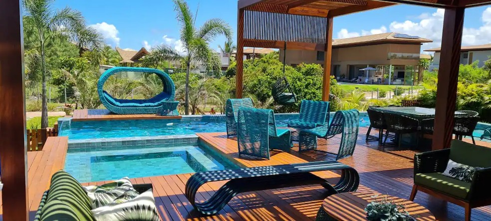 A área externa tem piscina e jacuzzi, além de diversas cadeiras e sofás para relaxar — Foto: Airbnb / Reprodução