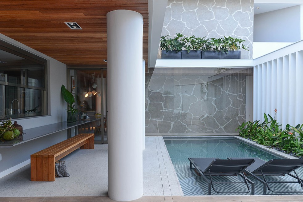 ÁREA EXTERNA | O revestimento da piscina é da Portinari. A passarela de vidro conecta a casa com o lavabo e quarto — Foto: Jana de Oliveira / Divulgação
