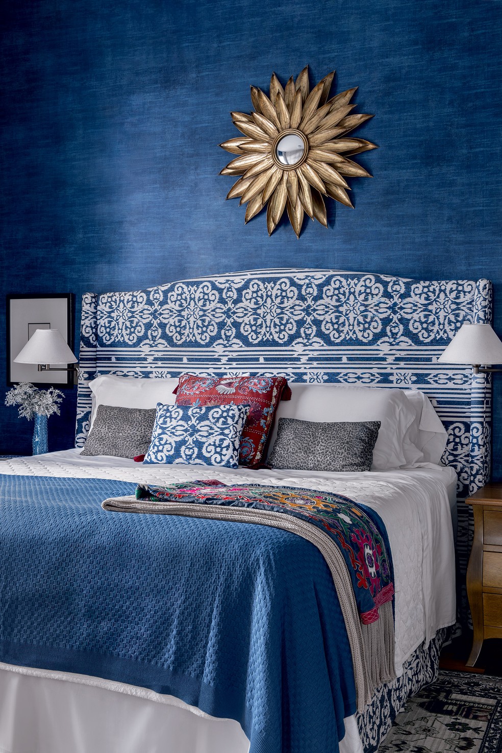 QUARTO | O papel de parede de intenso azul, da Paula Papéis e Tecidos, torna o ambiente aconchegante. A cabeceira da cama, revestida de tecido da Entreposto, é alta para trazer mais conforto. Arandelas da Golden-Art. Manta adquirida na By Kamy — Foto: Arq.verso/Divulgação