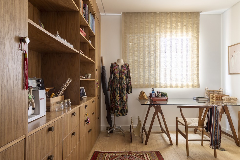 HOME OFFICE | O cômodo foi aberto para a sala e recebeu una grande estante de madeira com nichos para objetos decorativos — Foto: Evelyn Muller / Divulgação