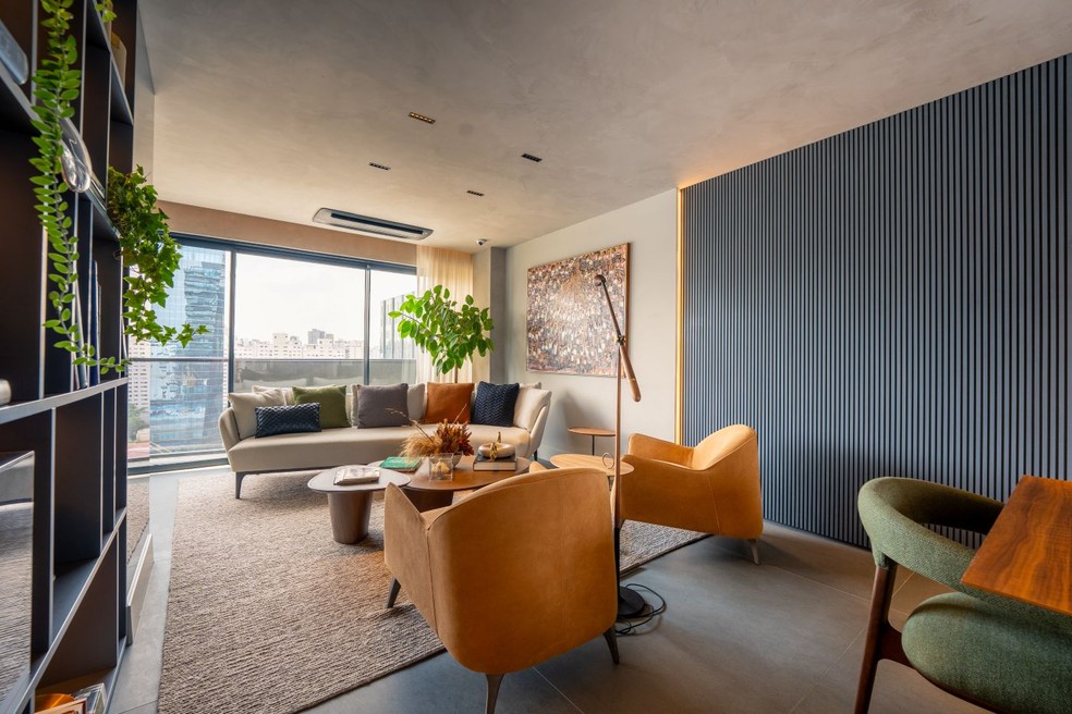 As linhas curvas marcam o mobiliário, com sofá Piero, poltronas Poline e mesa de centro Ginza, todos da Artefacto. Luminária de piso Memory, de Jader Almeida. O quadro é acervo do morador, adquirido em uma viagem. A estante foi executada com laminado BP Grafite, com iluminação embutida nas prateleiras horizontais, pela Florense, responsável também pelo painel ripado de MDF laqueado. Piso de Limestone Toscana levigado, da NPK Mármores. Tapete da by Kamy — Foto: Alexandre Suplicy/Divulgação | Projeto do arquiteto Carlos Rossi