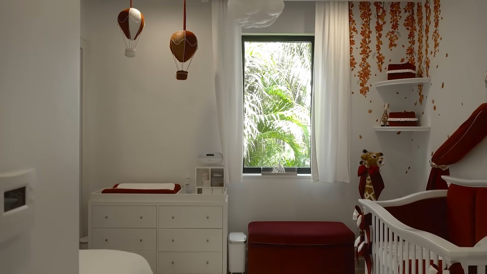 A decoração do quarto tem a presença das cores vermelho e branco, com uma janela e cortinas brancas — Foto: Youtube / Reprodução