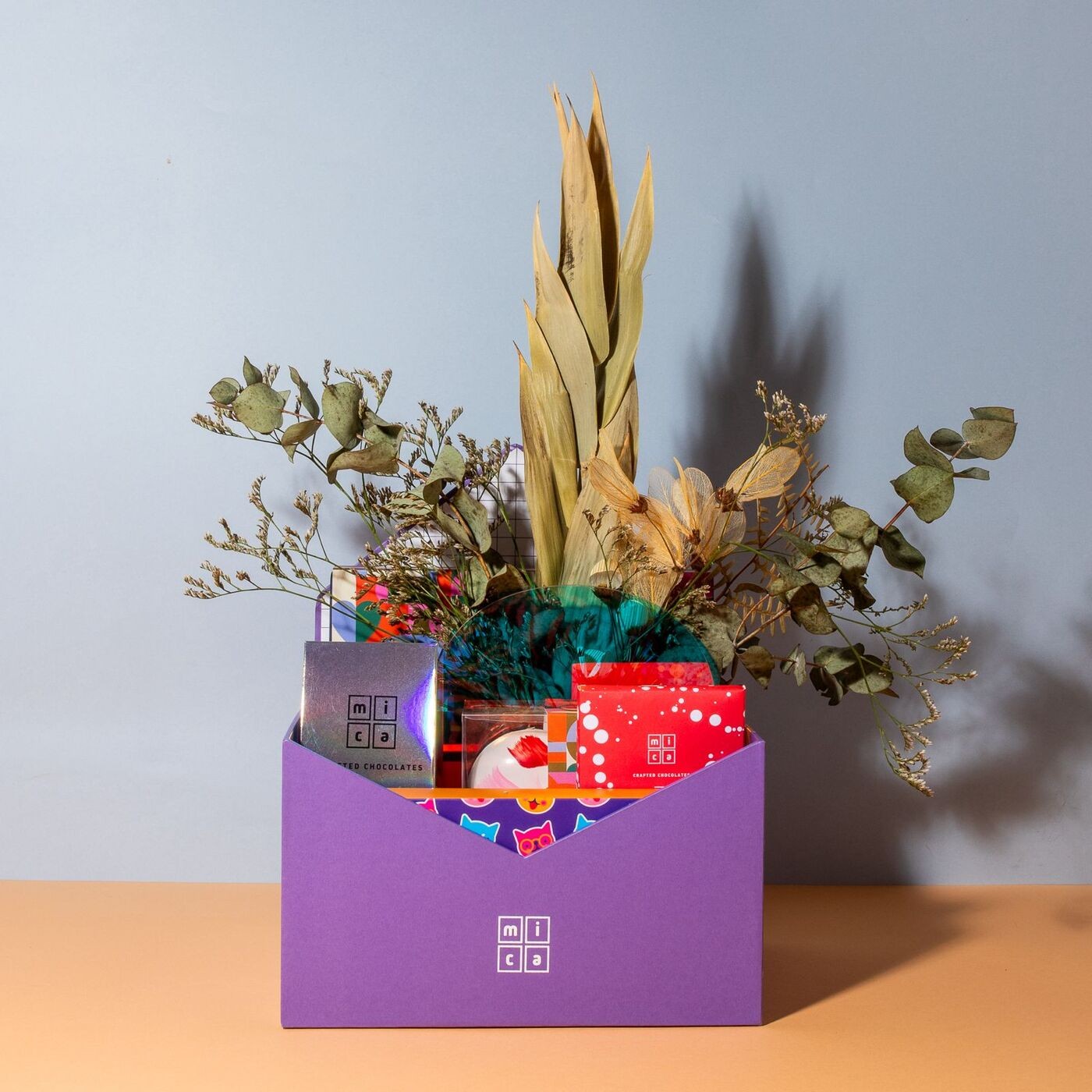 Caixa personalizada, da Mica, é montada em formato de envelope roxo com vaso de flores secas e chocolates escolhidos pelos clientes. O presente sai a partir de R$ 300 — Foto: Mica Chocolates / Divulgação