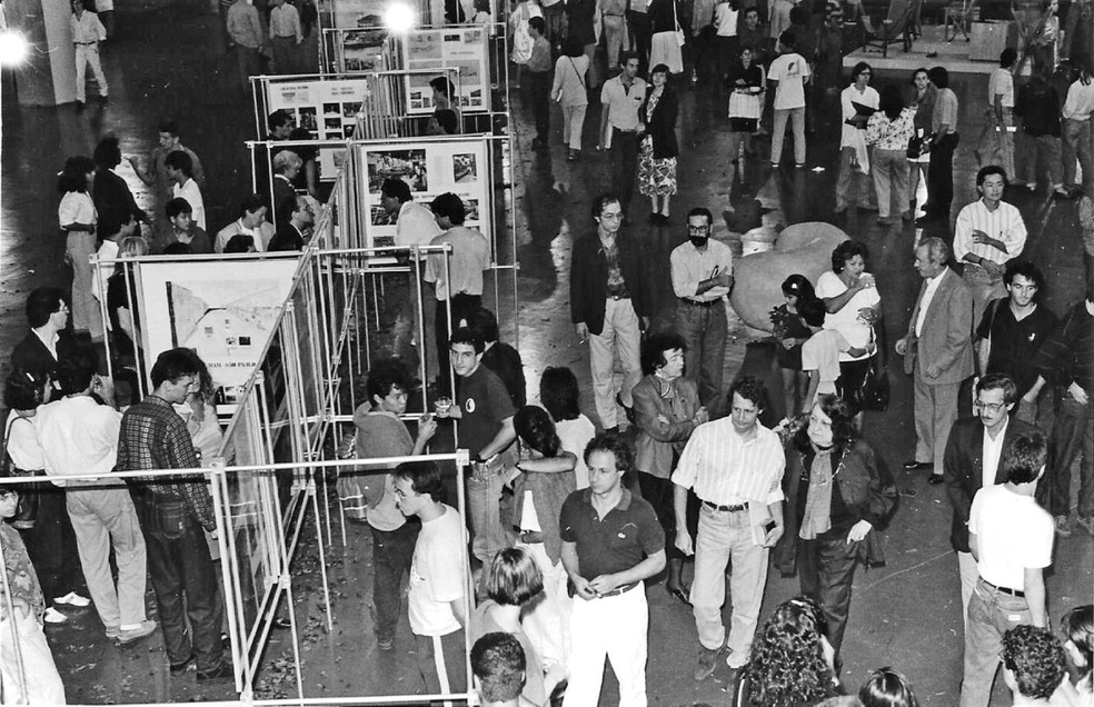 A exposição "Arquitetura e…" na Faculdade de Arquitetura e Urbanismo da Universidade de São Paulo em 1989 foi a primeira e única exposição em vida de Lina Bo Bardi. A arquiteta fez questão da presença do Polochon. Em primeiro plano, vemos Victor Nosek caminhando junto à Lina, que está de braços dados a Marcelo Ferraz e, logo atrás, o Polochon original usado na peça do Teatro do Ornitorrinco — Foto: Arquivo Pessoal / Victor Nosek