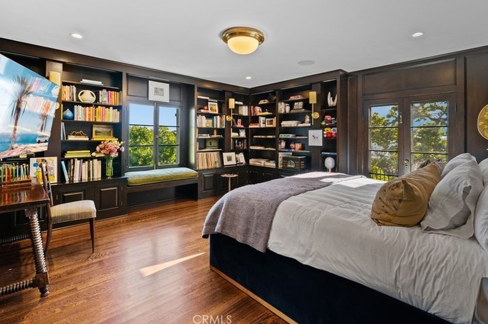 Um segundo quarto aconchegante tem piso de madeira e estantes com livros — Foto: Coldwell Banker / Reprodução