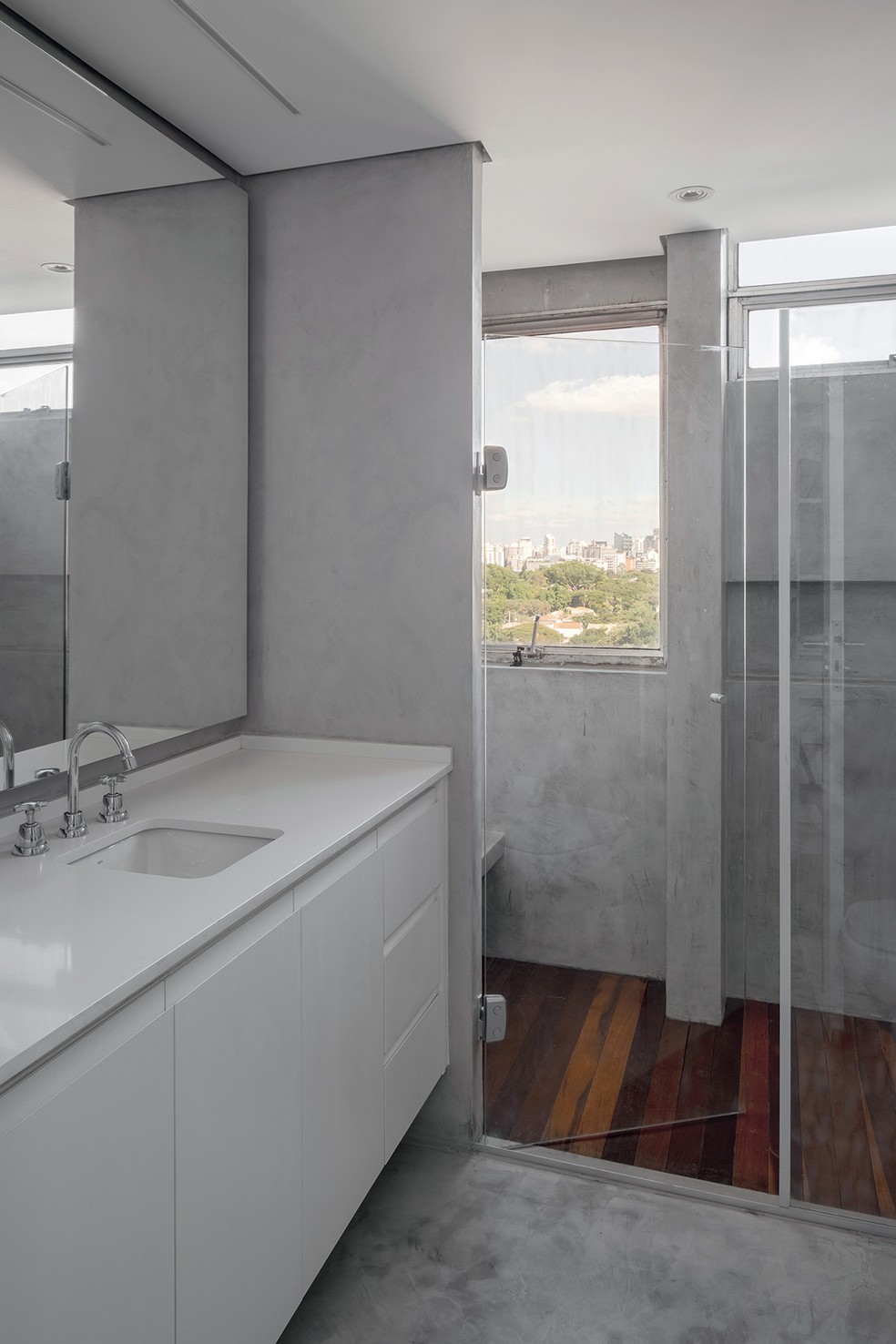 No banheiro, o cimento polimérico cobre o piso e as paredes. Bancada de quartzo branco e armário da Si Advisors — Foto: Carolina Lacaz / Divulgação