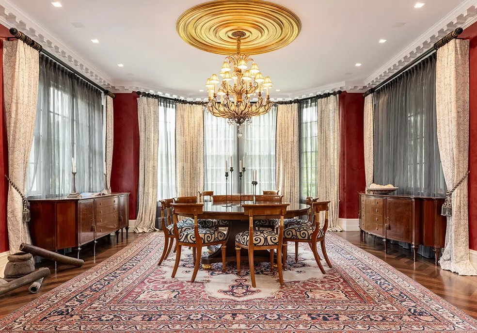 A sala de jantar tem uma mesa redonda de madeira e um lustre — Foto: Daniel Milstein for Sotheby’s International Realty / Reprodução