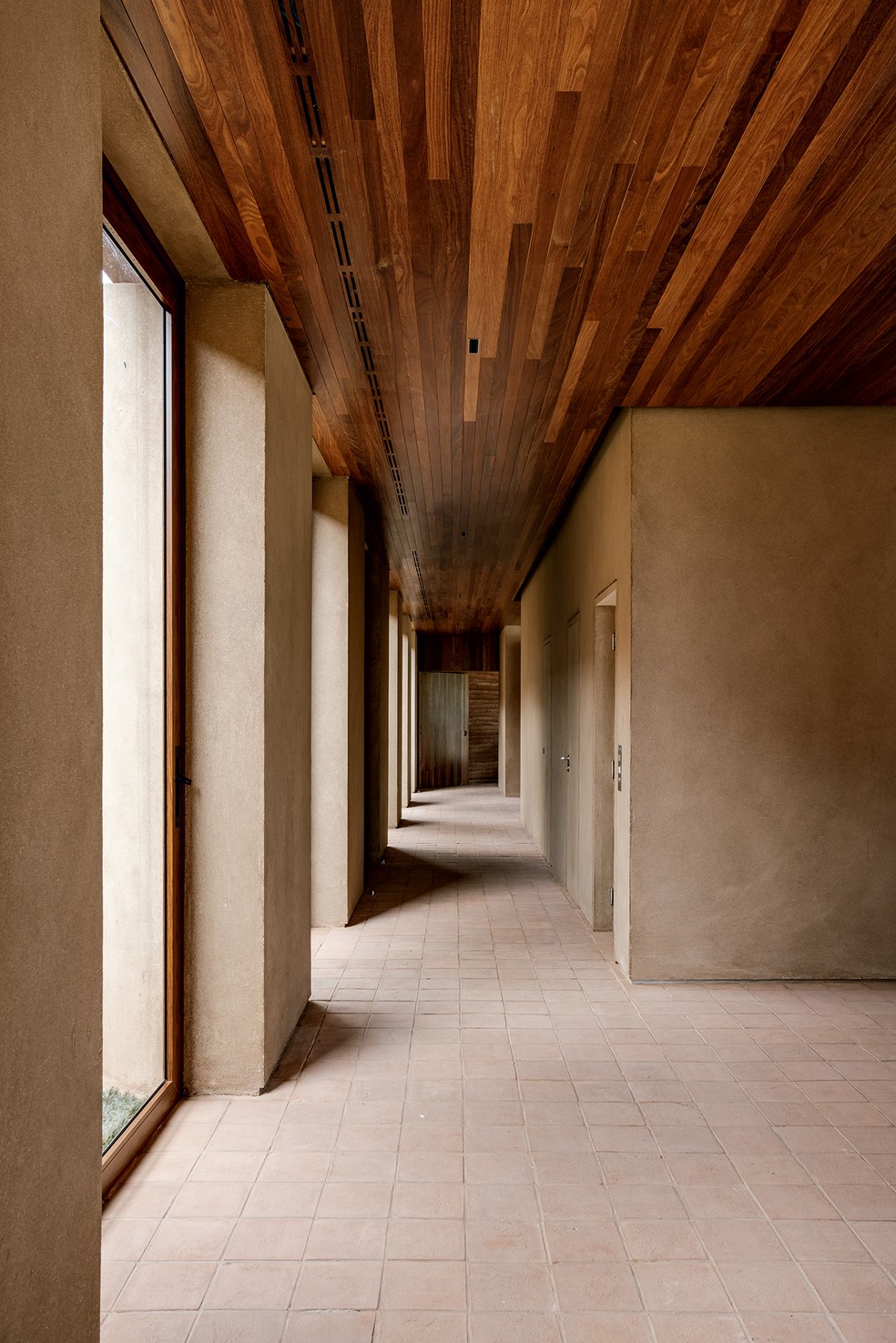 CORREDOR | O hall de circulação na entrada social da casa tem janelas pivotantes do piso ao teto com vidro em caixilho revestido de cumaru da Conceito Esquadrias de Alumínio — Foto: Fran Parente / Divulgação