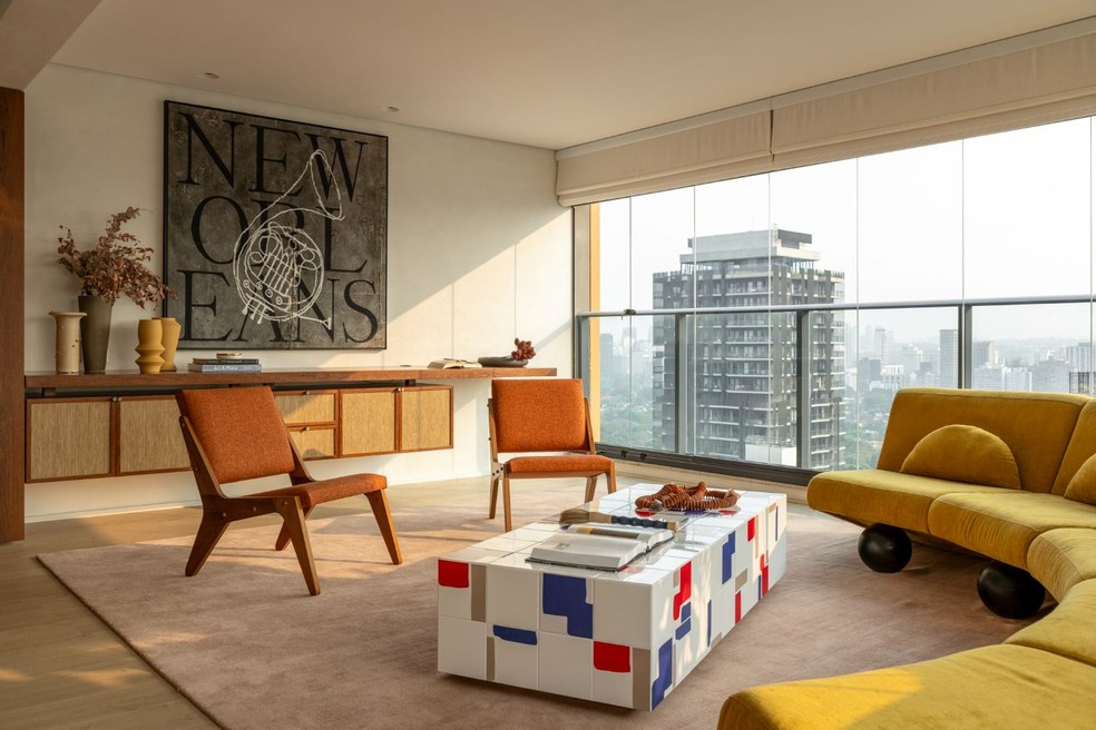 Cores quentes e design marcam o ambiente, com sofá curvo amarelo-mostarda, modelo Bardot, da Prototype, e par de poltronas terracota Zanine H, de Zanine Caldas. Projeto do Studio Julliana Camargo. — Foto: Leila Viegas/Divulgação