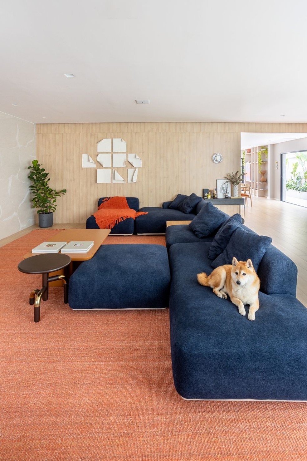 ESTAR | Cores e texturas se misturam no espaço, com sofá da Wood Mobili, onde está Zucco, cão da raça Shiba Inu. Tapete alaranjado da by Kamy. Mesas de centro da Breton. Ao fundo, no painel de MDF Carvalho Treviso, da Berneck, está a escultura do Studio Lupomo e a arandela assinada por Waldir Junior — Foto: Dam Mol/Divulgação