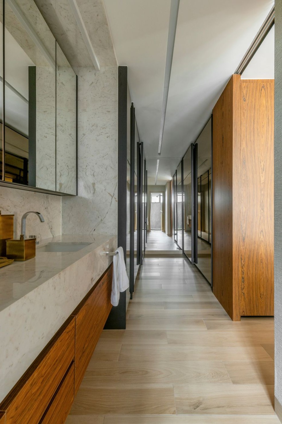 BANHEIRO | A suíte máster integra closet e bancada do lavatório, que é separado do banho e do sanitário. Bancada de mármore branco Paraná executada pela Gruta Mármores, enquanto a marcenaria em pau-ferro natural é da Casa Marista. Armários com portas em vidro refletivo realizados pela Terra Ambientes — Foto: Edgar Cesar/Divulgação