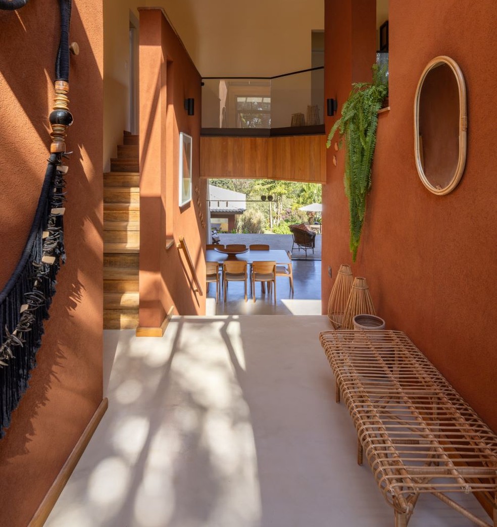 O corredor que leva à área social e ao mezanino pelas escadas tem banco de vime, espelho e lanterna, todos da Lili Home Decor — Foto: Manuel Sá/Divulgação | Projeto do escritório Sertão Arquitetos