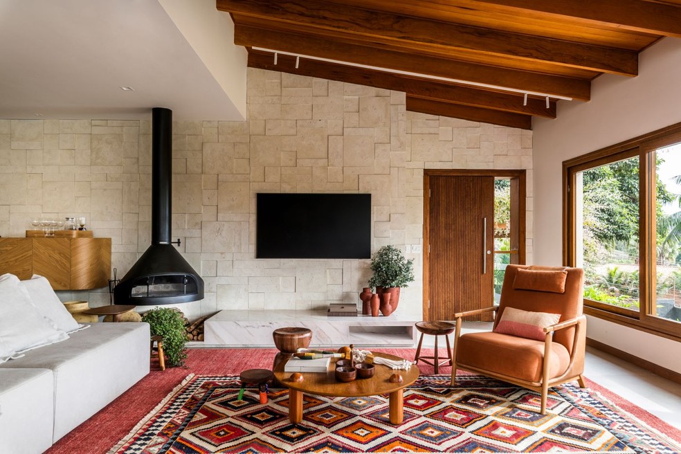 No projeto do escritório Pixel Arquitetura, o mármore Branco Paraná cria uma caixa, que faz as vezes de rack para a TV e tem nicho para armazenar as lenhas da lareira da Construflama — Foto: Renato Navarro/Divulgação